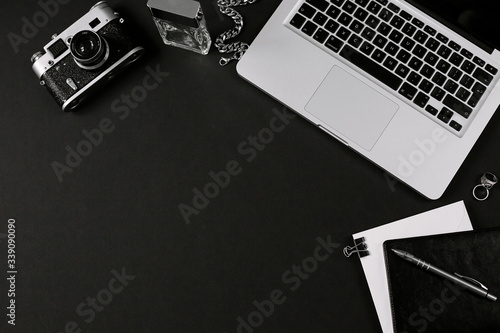 Framed mockup for business and freelance concept. Stylish workspace of designer with laptop, vintage film camera, notebook, headphones, pen and smartphone on black desk. Flat lay, top view
