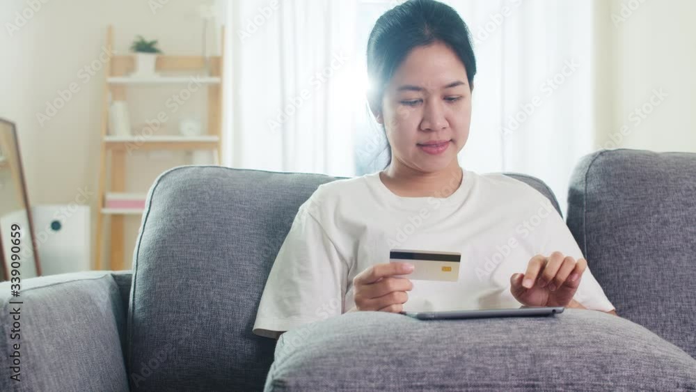Asian woman using tablet, credit card buy and purchase e-commerce internet in living room from home when social distancing stay at home and self quarantine time, online shopping, coronavirus concept. Asian woman using tablet, credit card buy and purchase e-commerce internet in living room from home when social distancing stay at home and self quarantine time, online shopping, coronavirus concept.