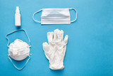 Disposable surgical mask, reusable medical respirator, latex gloves and alcohol sanitizer hand spray for cleaning hygiene protection corona virus or antibacterial, shot on blue background, top view.