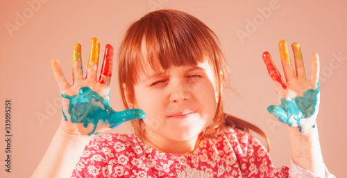 Fun pastime  art and baeuty concept. Colorful painted hands in a beautiful young girl. Funny facial expression of child.