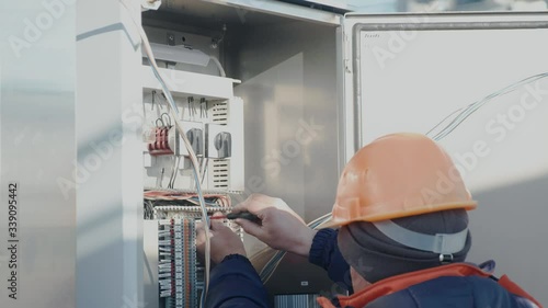 a male electrician works in a switchboard with an electrical connecting cable