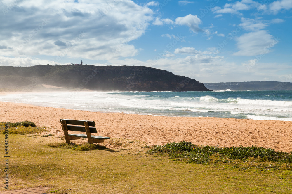 Wooden bench on the sandy beach next to the ocean, Atlantic ocean. Palm Beach, Sydney.
