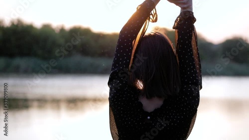 A girl in a black dress sits on the lake and looks at the sunset. View from the back. Rest, relaxation, sadness