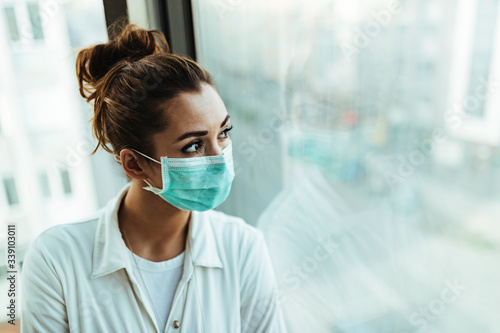 Pensive woman wearing face mask while looking through the window.