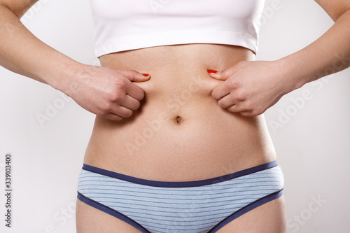 the woman pinches the excess fat on her sides and belly with her fingers.