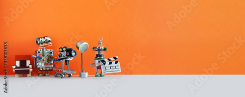 Robotic filmmaking backstage. Two robots shoots motion picture television episode or movie. Funny filmmakers director cameraman, cyborg assistant with clapperboard. Orange gray background, copy space photo