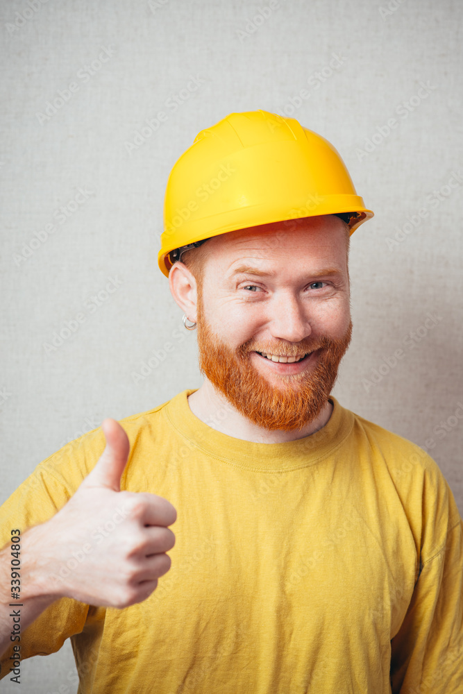 on a gray background man with a beard in a yellow shirt and yellow construction helmet showing thumbs up on a gray background man with a beard in a yellow shirt and yellow construction helmet showing thumbs up
