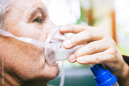 Senior man using medical equipment for inhalation with respiratory mask, nebulizer photo