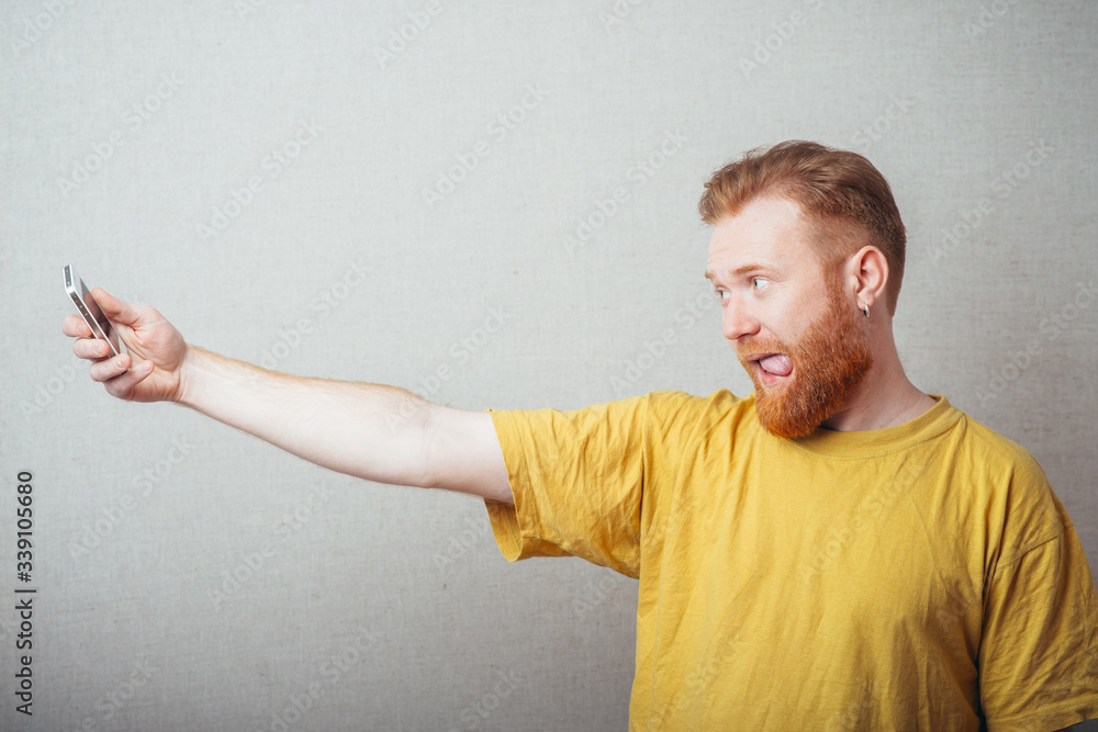 on a gray background man with a beard in a yellow T-shirt photo of yourself on your mobile phone on a gray background man with a beard in a yellow T-shirt photo of yourself on your mobile phone