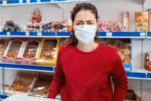A portrait of woman in a medical mask, with a malicious expression on her face. In the background are shelves of the store. The concept of coronovirus and the crisis in business