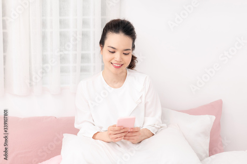 Cheerful teengaer uses mobile phone for online chatting, networking, recieves text message in bed