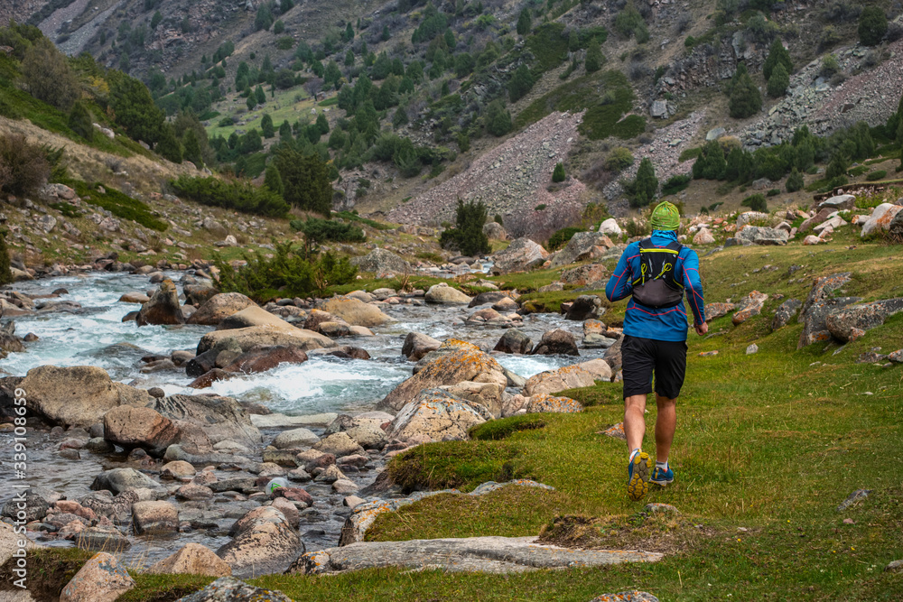 Runner guy is jogging in the highlands. Athlete runs near a mountain river. Man is training outdoors. Trail running