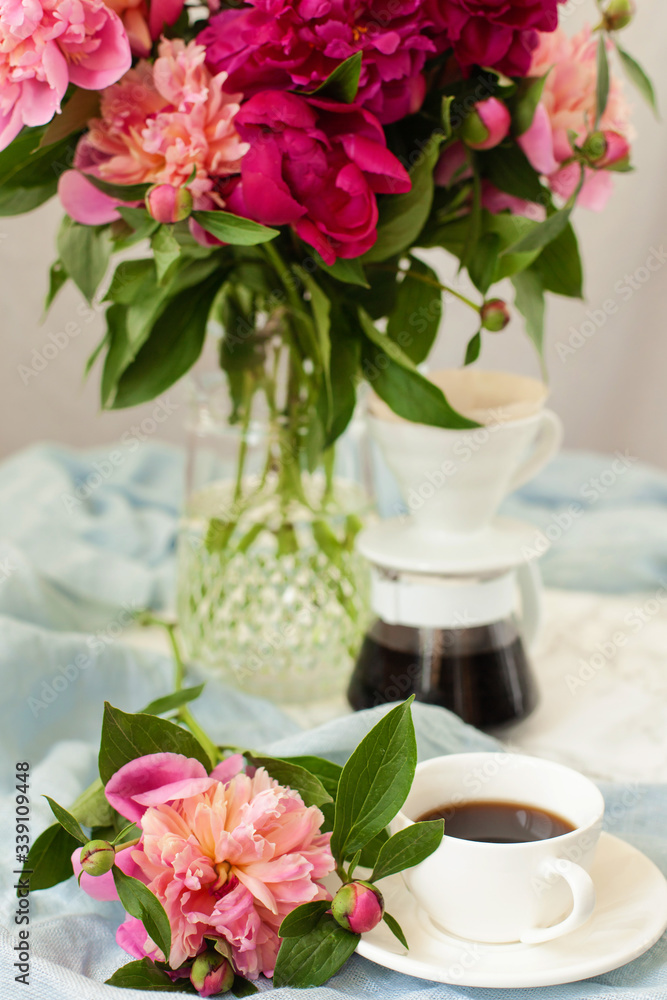 Spring or summer still life with beautiful flowers, drinks and light cloth on the table. Lush bouquet of pink and red peonies, pourover for making filter coffee and cup of hot espresso Spring or summer still life with beautiful flowers, drinks and light cloth on the table. Lush bouquet of pink and red peonies, pourover for making filter coffee and cup of hot espresso