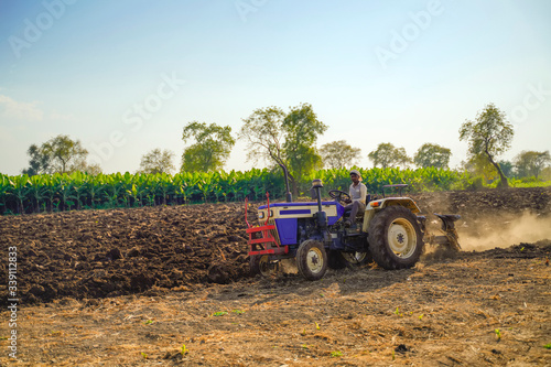 Indian / Asian farmer with tractor preparing land for sowing with cultivator, An Indian farming scene.