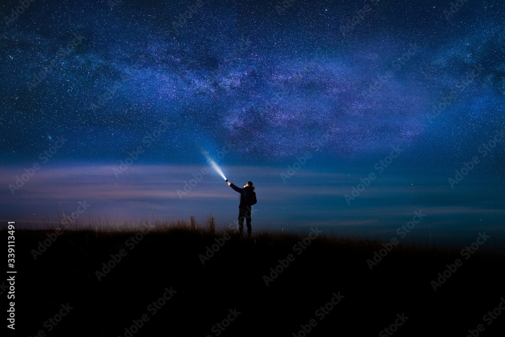 Fototapeta premium Night sky with Milky Way and silhouette of a standing happy man with classic blue light. Image soft focus and noise due to long expose and high iso.