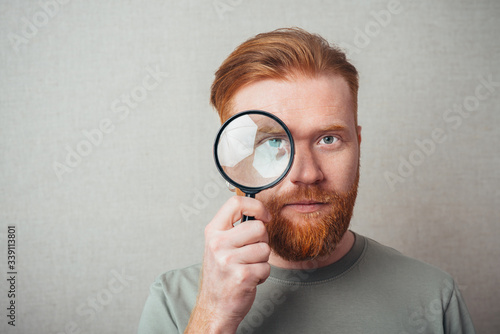 Young hipster red bearded man with magnifying glass