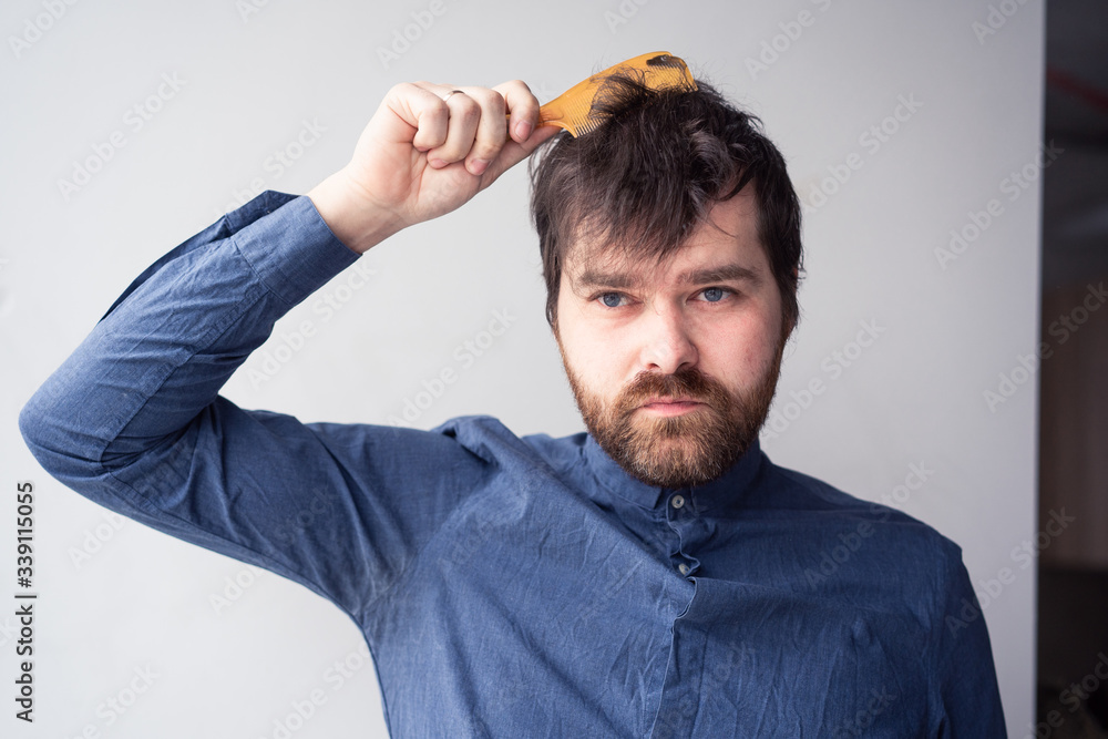 man with a comb in his hands combing his hair in a shirt on a light background man with a comb in his hands combing his hair in a shirt on a light background