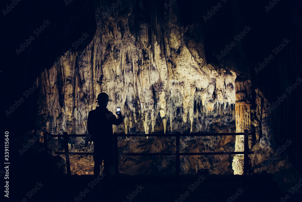 Silhouette of a man taking pictures in a cave with smartphone.