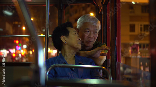 Asian elder couple have fun travel through Hong Kong city tram at night light