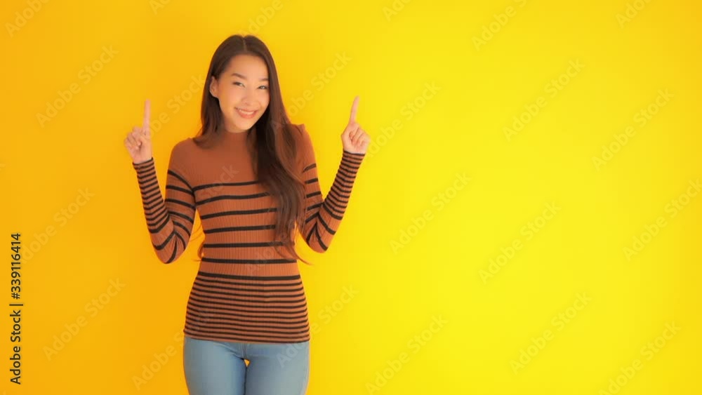 Smiling Asian girl holding up both fingers pointing upwards. Copy Space Yellow Background. Smiling Asian girl holding up both fingers pointing upwards. Copy Space Yellow Background.
