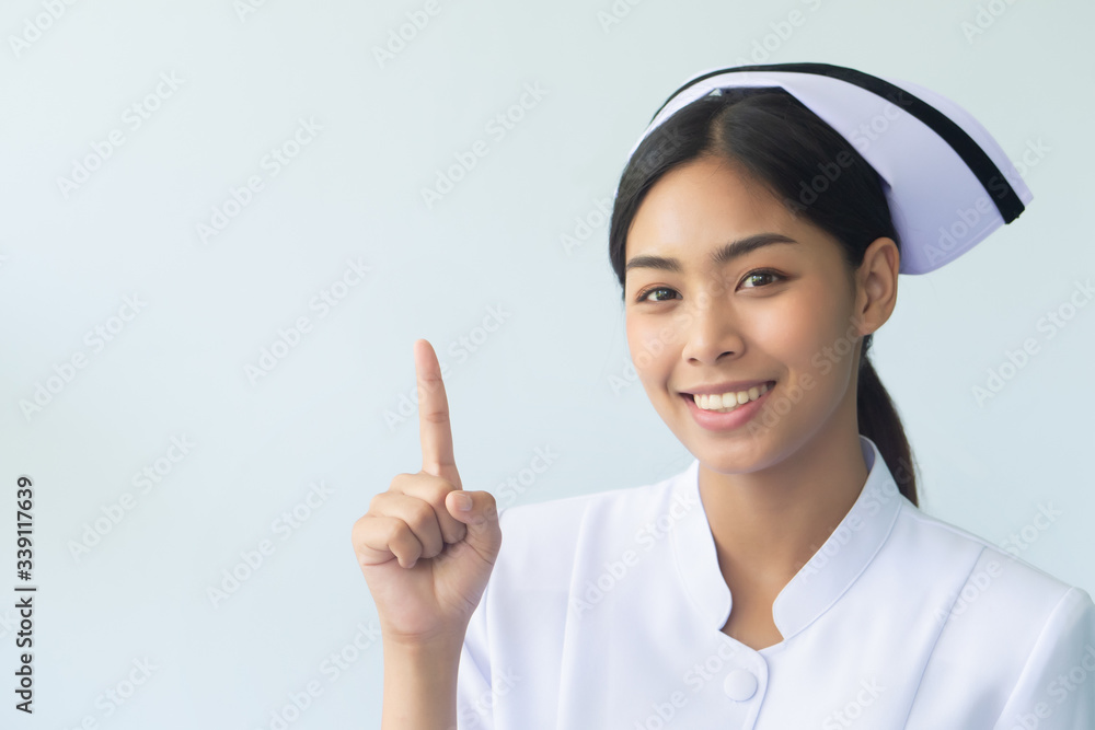 portrait of happy smiling asian woman nurse isolated pointing her finger to blank space; confident and friendly female nurse or medical worker pointing one finger up portrait of happy smiling asian woman nurse isolated pointing her finger to blank space; confident and friendly female nurse or medical worker pointing one finger up