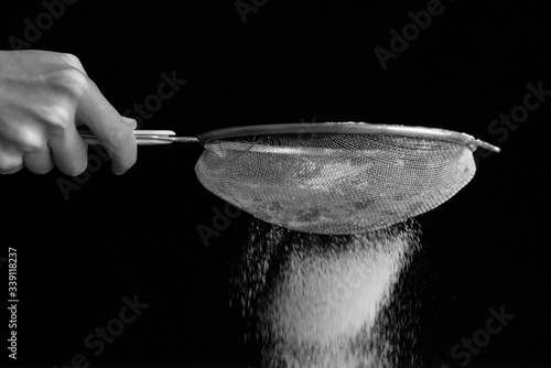 Fotografie Sifting flour through a sieve on the black background closeup