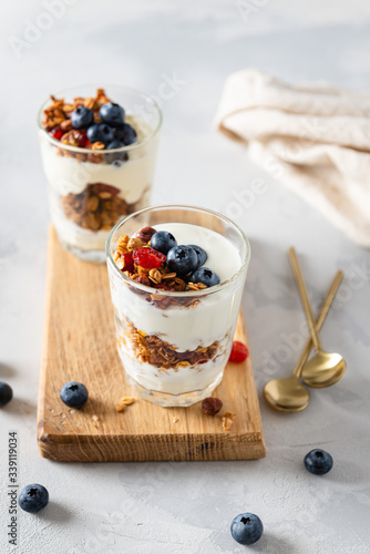 Homemade granola with honey, oatmeal, cashew nut, almond, hazelnut, walnut, raisin and cranberry in glassesl with yogurt on light concrete background, side view photo