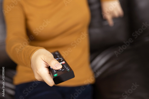 close up Television remote control in casual young female yellow shirt hands pointing to tv set and turning it on or off. select channel watching tv on sofa at home in the living room relax.