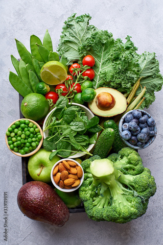 Creative flat lay with healthy vegetarian meal ingredients. Raw food concept. A variety of organic fruits  nuts  berries and vegetables in wooden box on concrete background