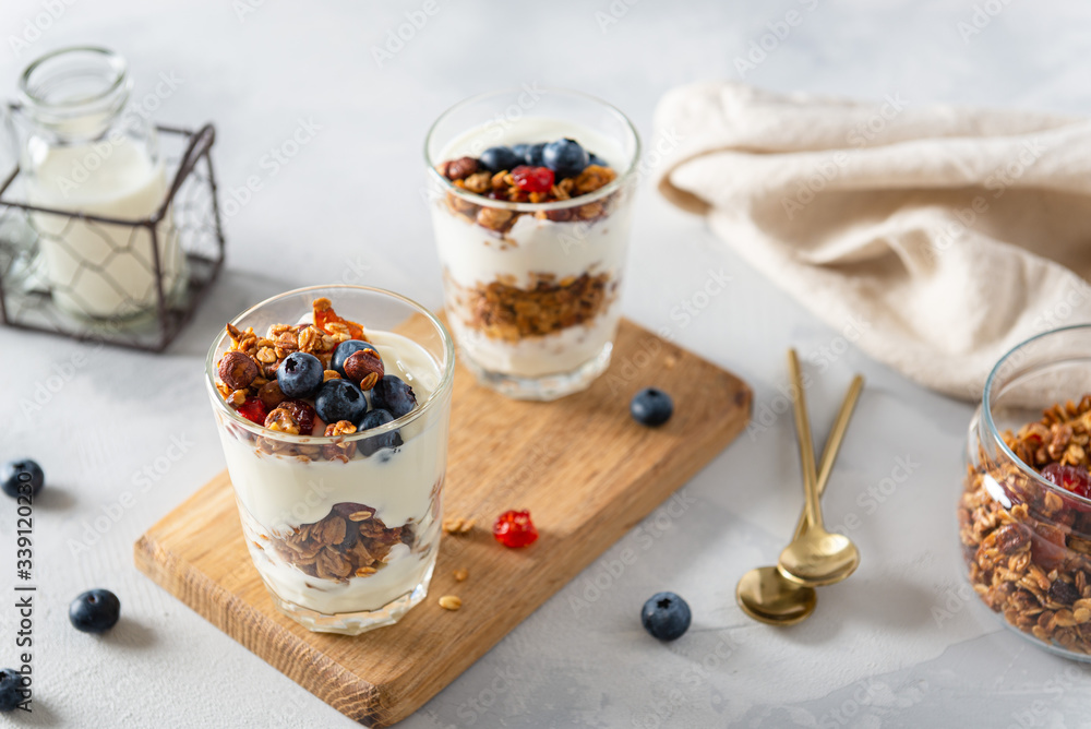 Crunchy honey granola with yogurt in glasses on white background. Dry breakfast cereals with flax seeds, cranberries and nuts. Healthy, vegeterian fiber food. Breakfast time. Dieting. Copy space Crunchy honey granola with yogurt in glasses on white background. Dry breakfast cereals with flax seeds, cranberries and nuts. Healthy, vegeterian fiber food. Breakfast time. Dieting. Copy space