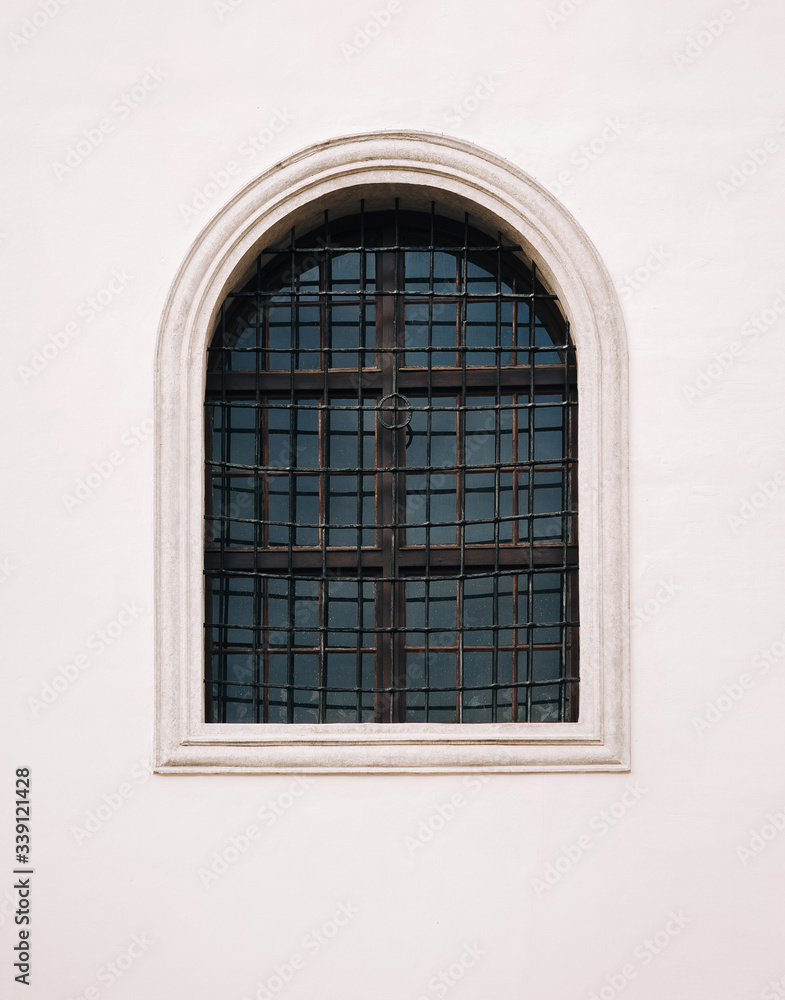 Antique old window with iron bars framed on a gray wall. The Jesuit Church in Lviv.