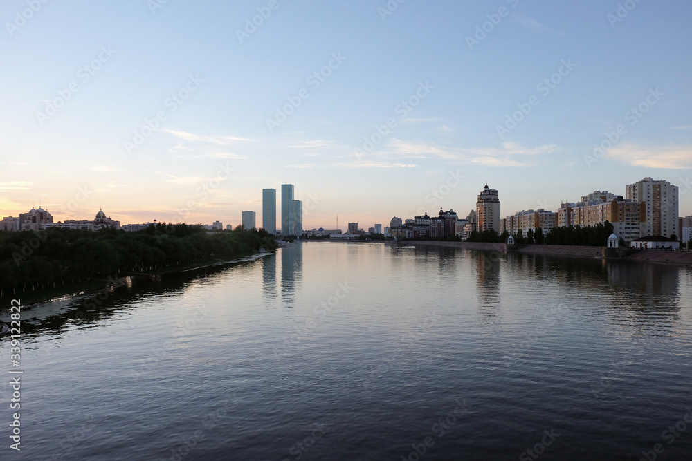 NUR-SULTAN, ASTANA, KAZAKHSTAN - JUNE 3, 2015: A beautifula panorama of Ishim river with smooth surface of water and evening city view