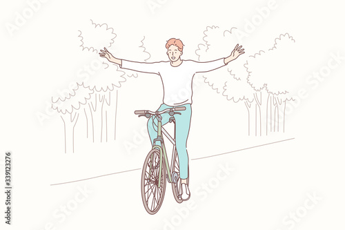 Cycling in park, freedom, lifestyle concept. Young happy smiling boy teenager student or man cyclist indulges in bicycling without hands in park. Outdoor sport activity healthy lifestyle leisure time.