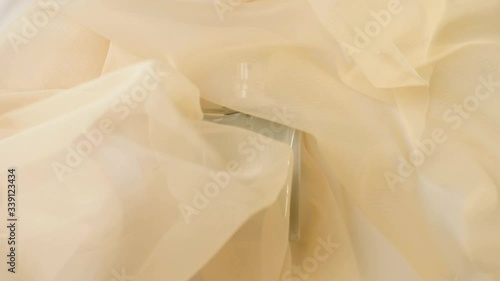 Flat surfaced bottle with cyan perfumes or essential oils is on the beige cloth. Beige fabric flutters around and waves around the bottle. Concept of aroma and smell. Close up. Slow motion