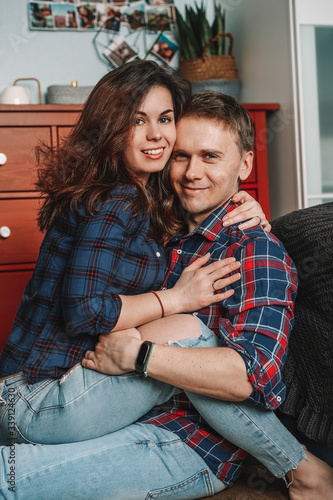 A couple in love, a friendly family are sitting next to the bed, in a beautiful home cozy interior, in the background a red chest of drawers, a man and a woman in plaid shirts