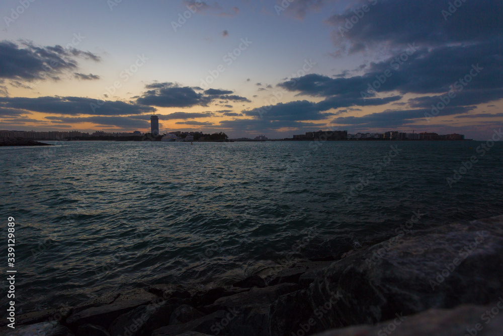Rising sun on the horizon above a calm ocean or sea. On the blue sky white clouds Rising sun on the horizon above a calm ocean or sea. On the blue sky white clouds