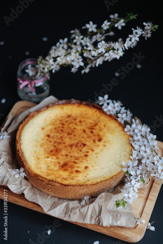 Tasty homemade cheesecake on wooden board and black table with blooming branch.