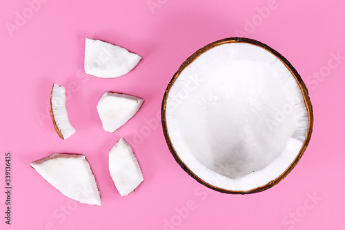 Open half of whole coconut fruit with cut pieces next to it on pink background