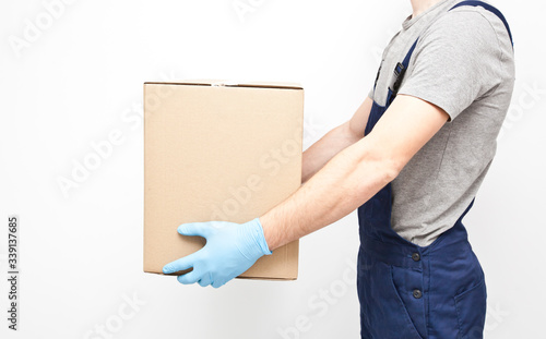 The courier is holding the carton box in his hand wearing  protective latex gloves on the gray background © SkyLine