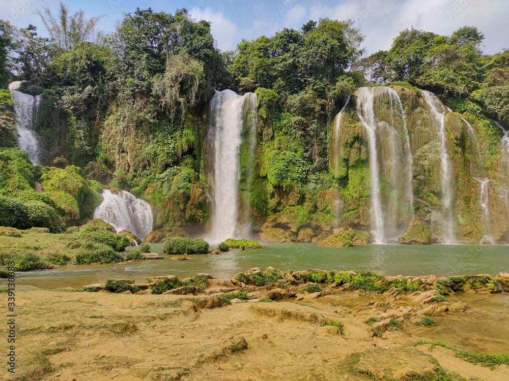 Obraz premium Full of water huge waterfall near the green forest with green trees in mountains