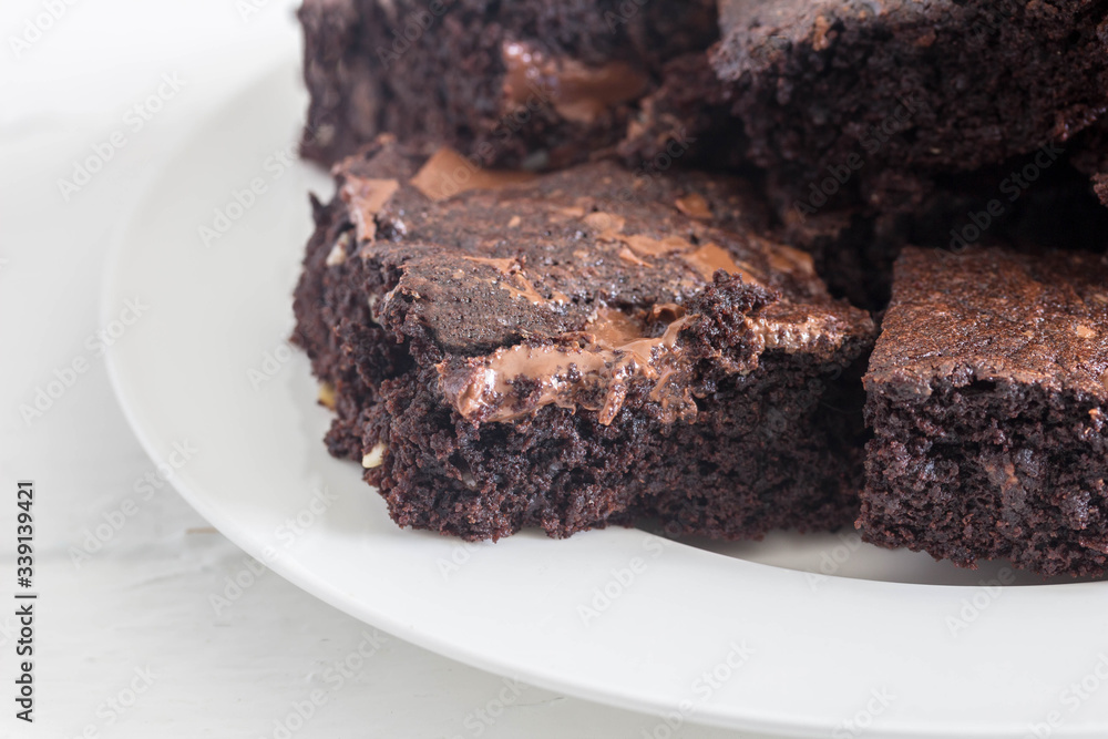 Chocolate brownies with melted chocolate bits stacked in a white plate close up with copy space