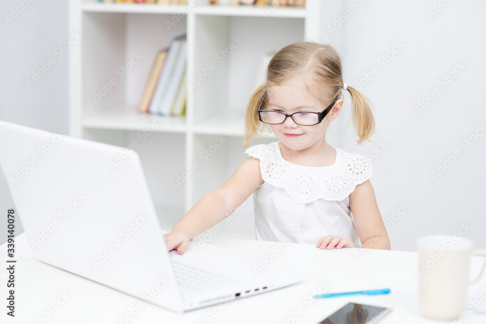 A little girl with glasses is engaged in distance learning using a laptop at home in the bedroom. Distance Learning during Quarantine Concept A little girl with glasses is engaged in distance learning using a laptop at home in the bedroom. Distance Learning during Quarantine Concept