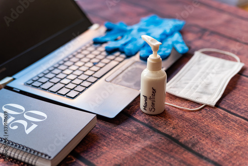 hand sanitizer work from home kit on wooden office desk with computer and face mask, a solution against the spread of corona virus for quarantined employees photo