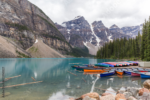 canoes of different colors docked on a jetty of a turquoise water lake with high mountains on a cloudy day