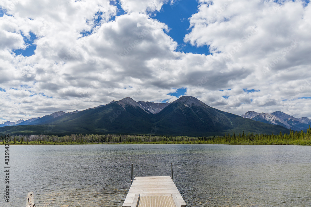 jetty on a dark water lake, background mountains and blue sky with white clouds