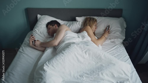 Heterosexual couple having problem in bed. Trouble in relationship. They are addicted to phone and don't look at each other. Husband and wife lying apart. Marriage, Fabbing, family, love, sex concept. photo