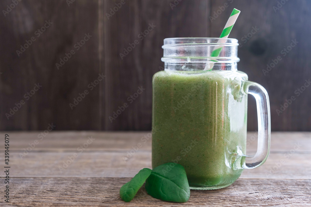 One glass with a pen with a fresh green smoothie of celery, spinach and apple on an old wooden table. Nearby are two green spinach leaves. Place for text One glass with a pen with a fresh green smoothie of celery, spinach and apple on an old wooden table. Nearby are two green spinach leaves. Place for text