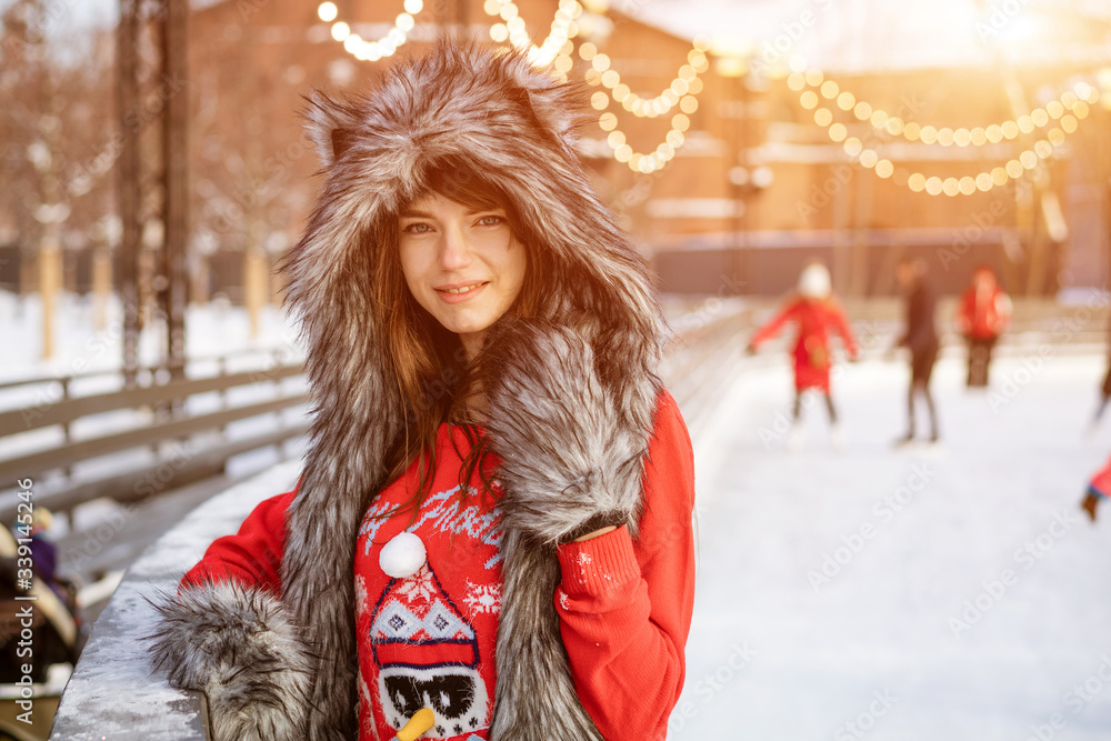 Happy young woman in a wolf hat in winter on the ice rink posing in a red sweater