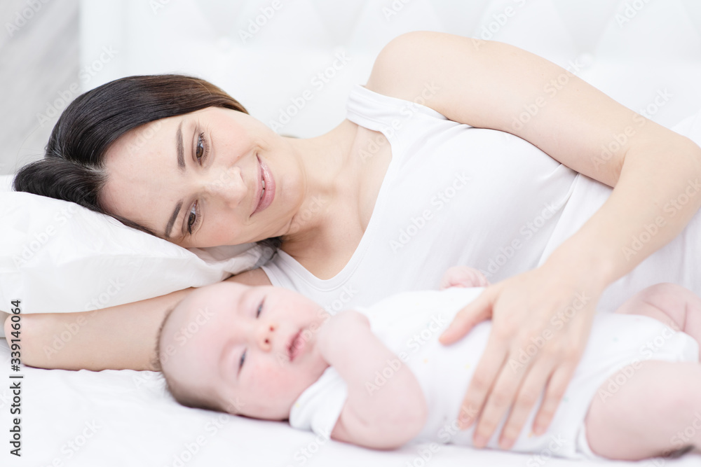Mother and child on a white bed. Mom and baby boy in diaper playing in sunny bedroom. Mother and child on a white bed. Mom and baby boy in diaper playing in sunny bedroom.