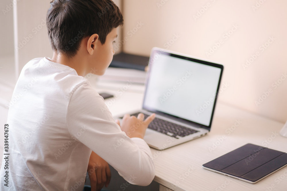 Schoolboy at home using laptop when studying. Teenage boy make homework on quarantine. Mockup Schoolboy at home using laptop when studying. Teenage boy make homework on quarantine. Mockup